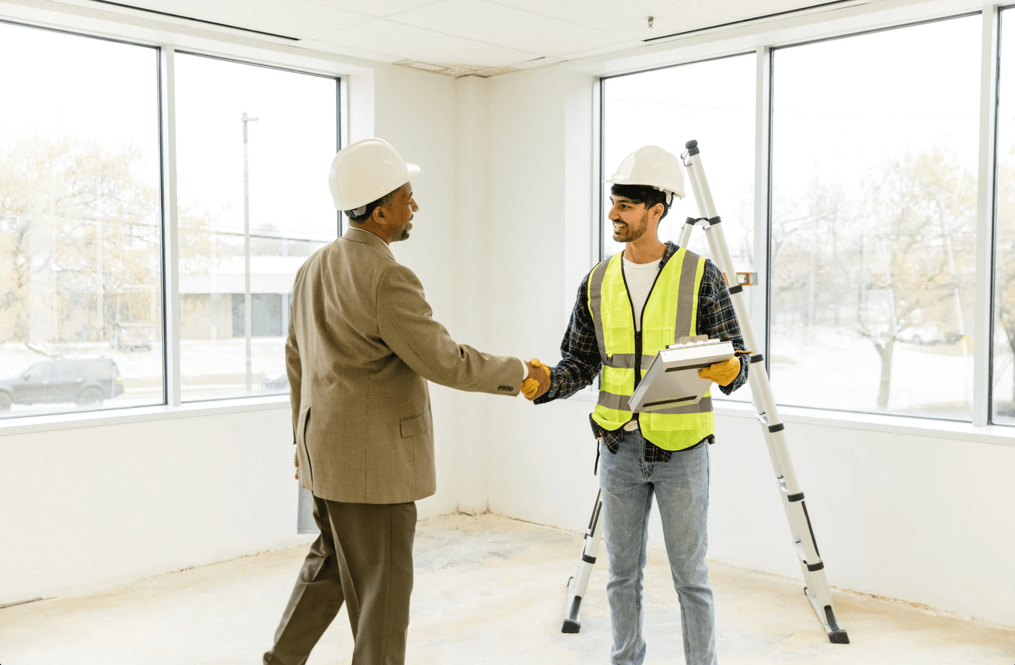 Two construction professionals shaking hands on site inside a building under construction