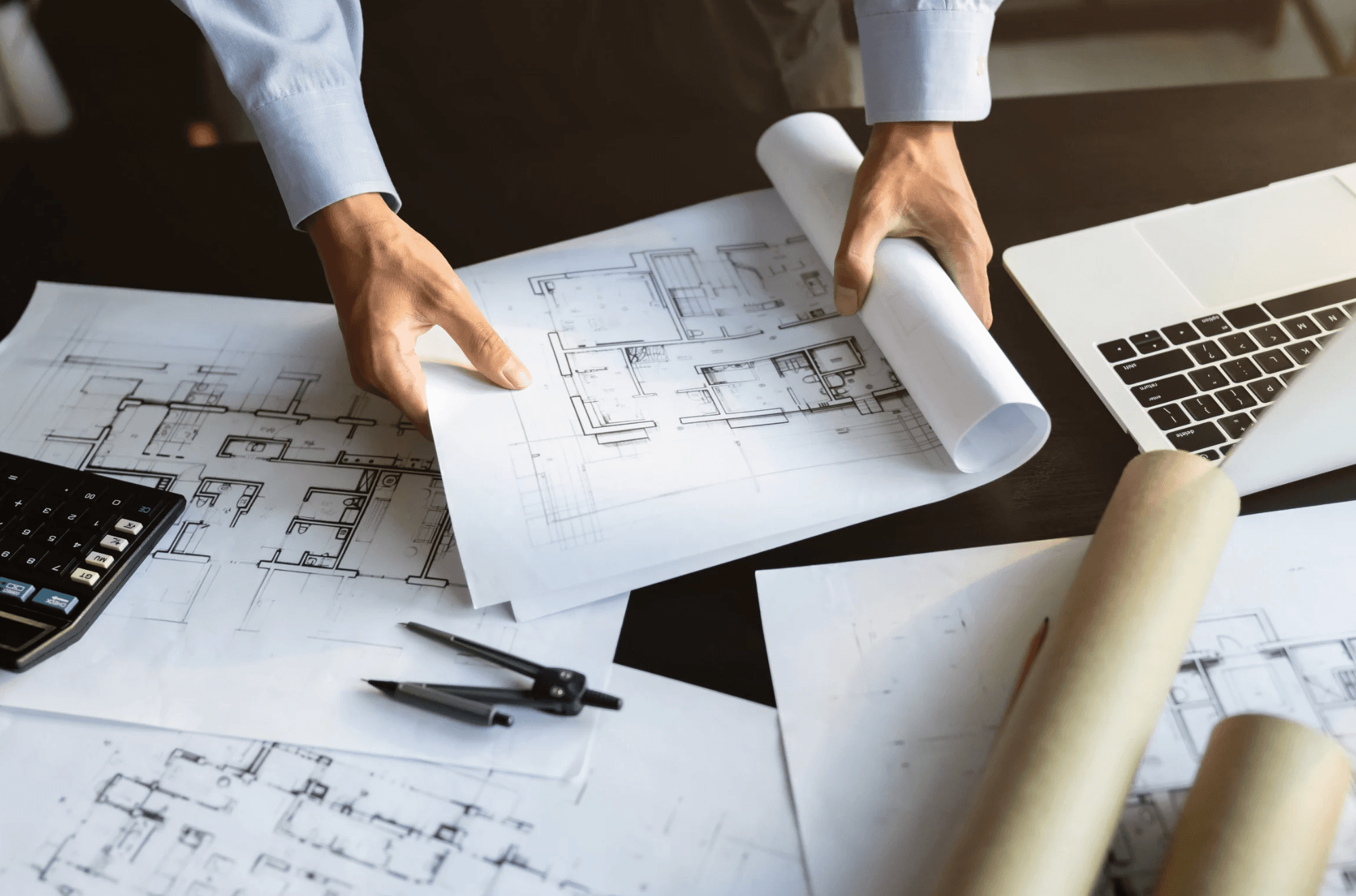 Architect reviewing blueprints on a desk with drafting tools and rolled plans